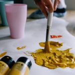 crop faceless artist sopping paintbrush in yellow paint
